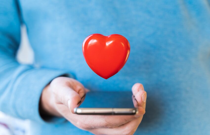 Big flying red heart. Mobile phone, smartphone in hand of man. Valentine's day holiday concept.Onlin