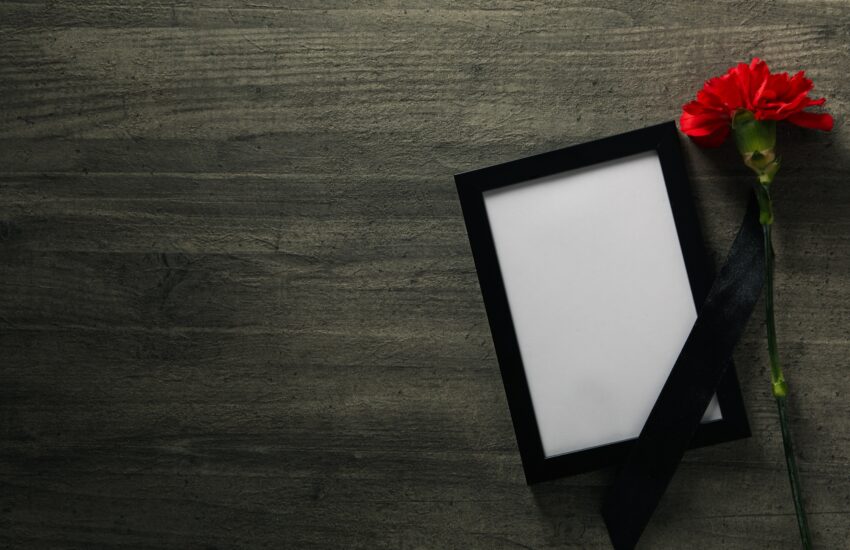 Photo frame with black ribbon and flower on wooden background, space for text