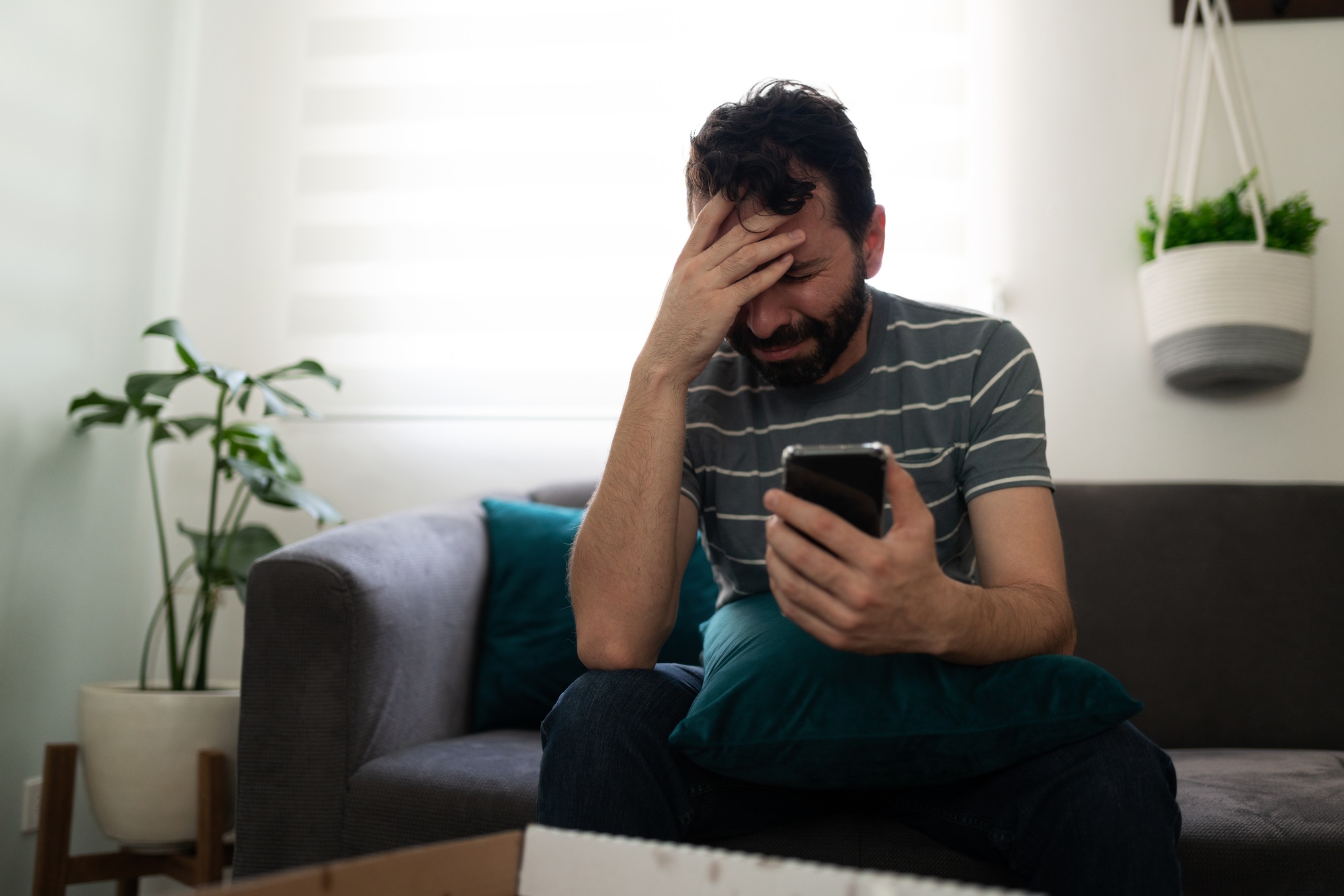Adult man crying and looking sadly at a message on his smartphone